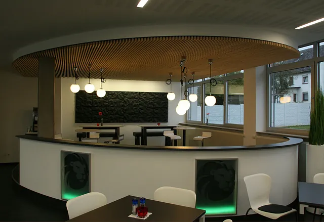 Modernes Café-Interieur mit geschwungener Bar, kugelförmigen Pendelleuchten und Holzdecke.