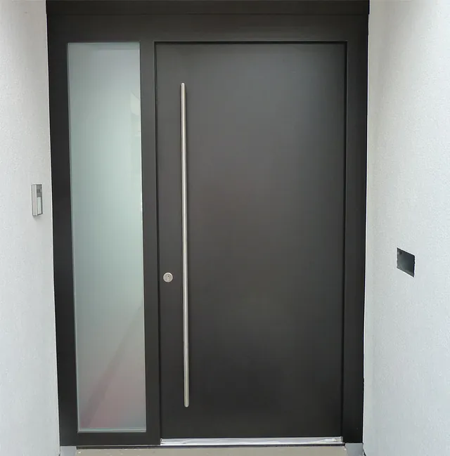 Schwarze Haustür mit langem, schmalem Griff und seitlichem, mattiertem Glasfenster.