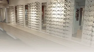 Wand mit mehreren Reihen von Brillenfassungen in einem Geschäft, beleuchtet und geordnet auf Regalen.