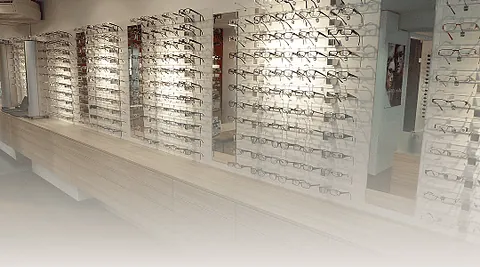 Wand mit mehreren Reihen von Brillenfassungen in einem Geschäft, beleuchtet und geordnet auf Regalen.