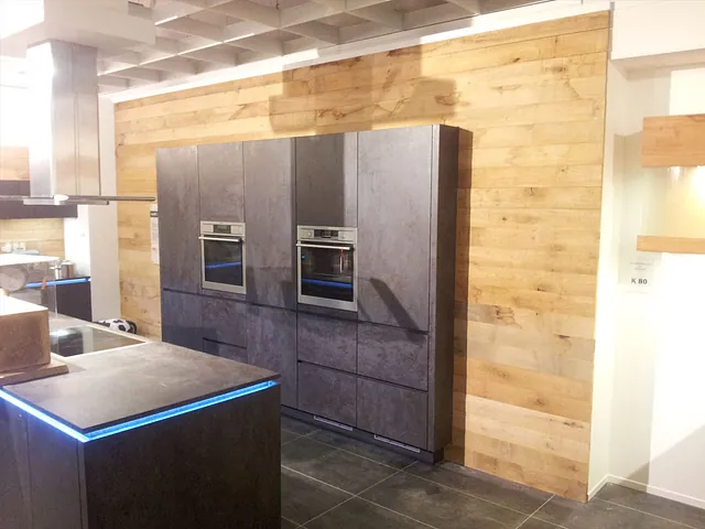 Moderne Küche mit dunklen Einbauschränken, zwei eingebauten Backöfen und Holzverkleidung an der Wand.