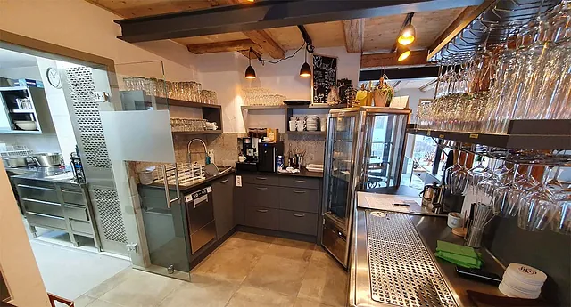 Moderne Küche mit grauen Schränken, Edelstahlspüle, Gläsern auf Regalen und offenem Kühlschrank.