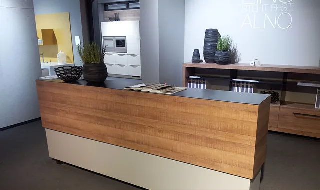 Ein moderner Küchenausstellungsraum verfügt über eine Kücheninsel aus Holz mit einer dunklen Arbeitsplatte.