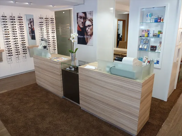 Empfangstresen in einem Optikergeschäft mit Brillenständern an der Wand und Regalen mit Produkten.