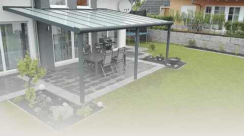 Terrasse mit Glasüberdachung, darunter Tisch mit Stühlen und Grill, umgeben von Garten mit Rasen und Beeten.