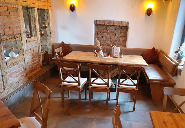 Ein Esstisch aus Holz mit gepolsterten Sitzbänken und Holzstühlen in einem gemütlichen Restaurant mit Ziegel- und Putzwänden.