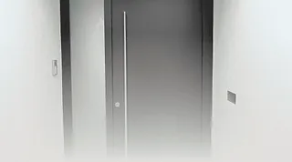 Haustür mit Griff in einem schmalen Flur mit weißer Wand und Lichtschalter.